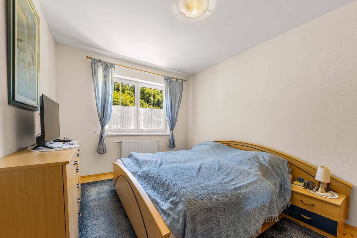 Helles Schlafzimmer mit Holzbett, Teppichboden und Blick ins Grüne.