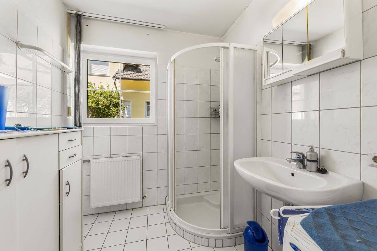 Funktionales Badezimmer mit Duschkabine, weißen Fliesen und Fenster.