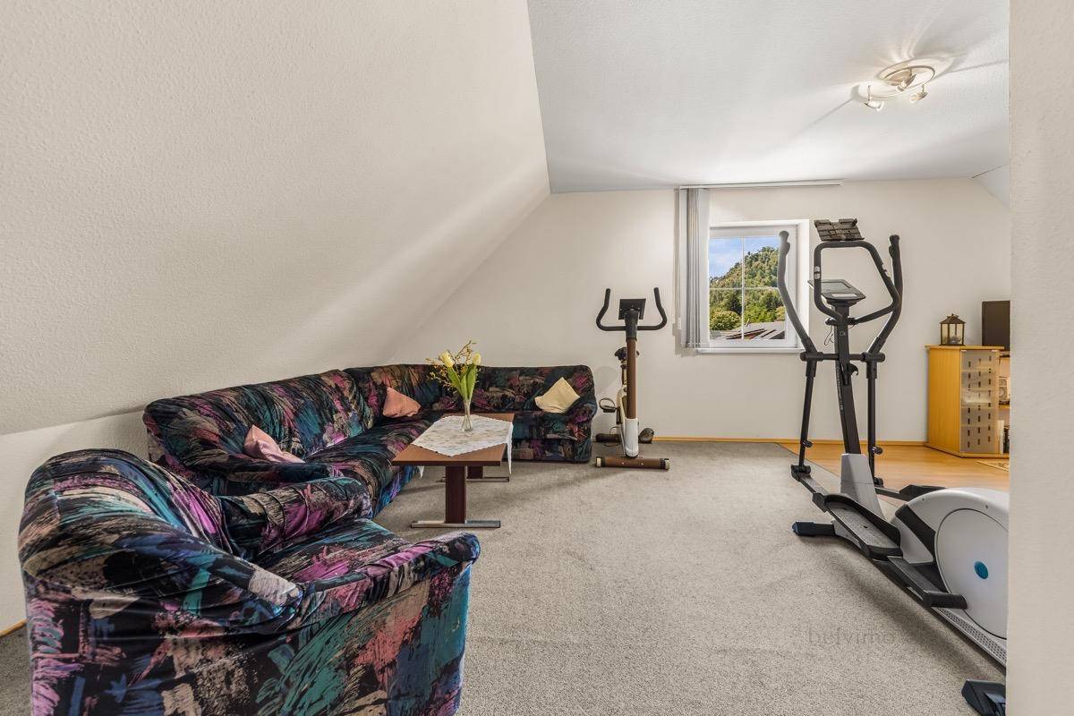 Geräumiger Dachbodenbereich mit Teppichboden, Sitzgelegenheiten und Fitnessgeräten.