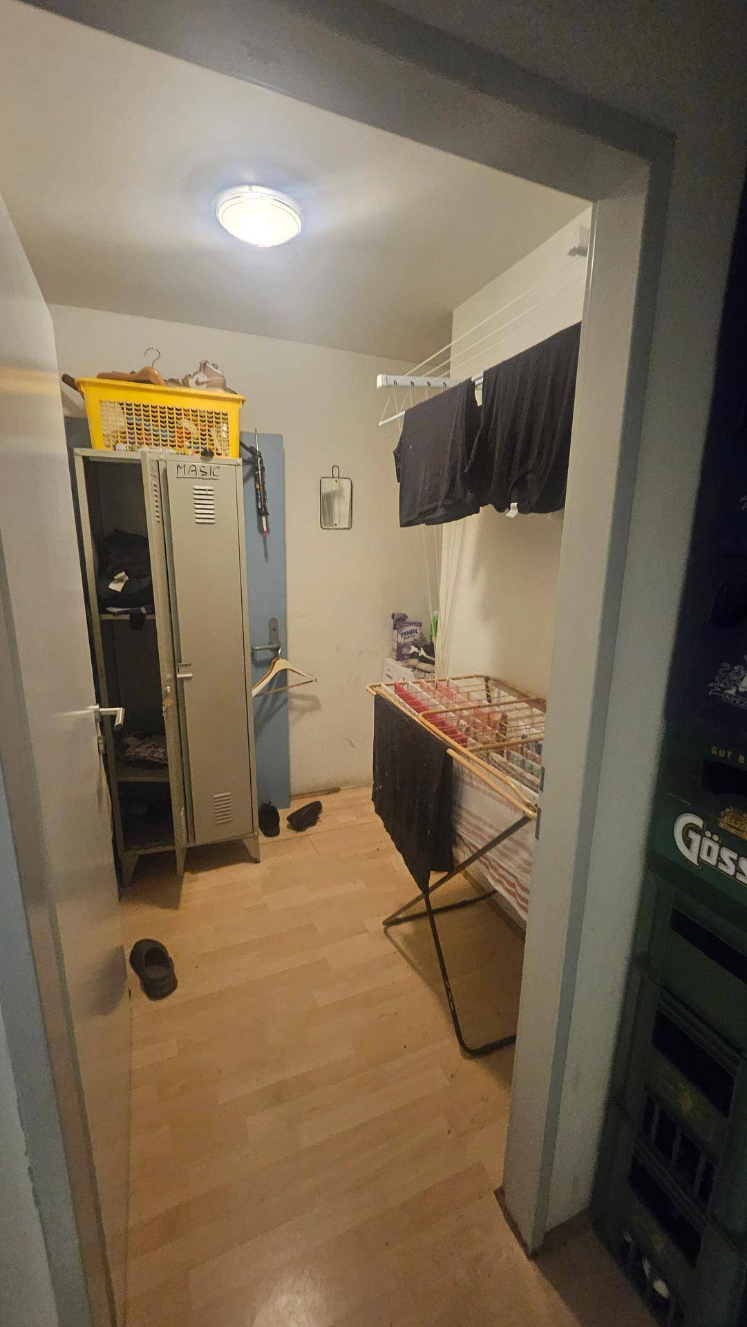 Kleiner Waschraum mit Wäscheständer, Spind und einfacher Beleuchtung.