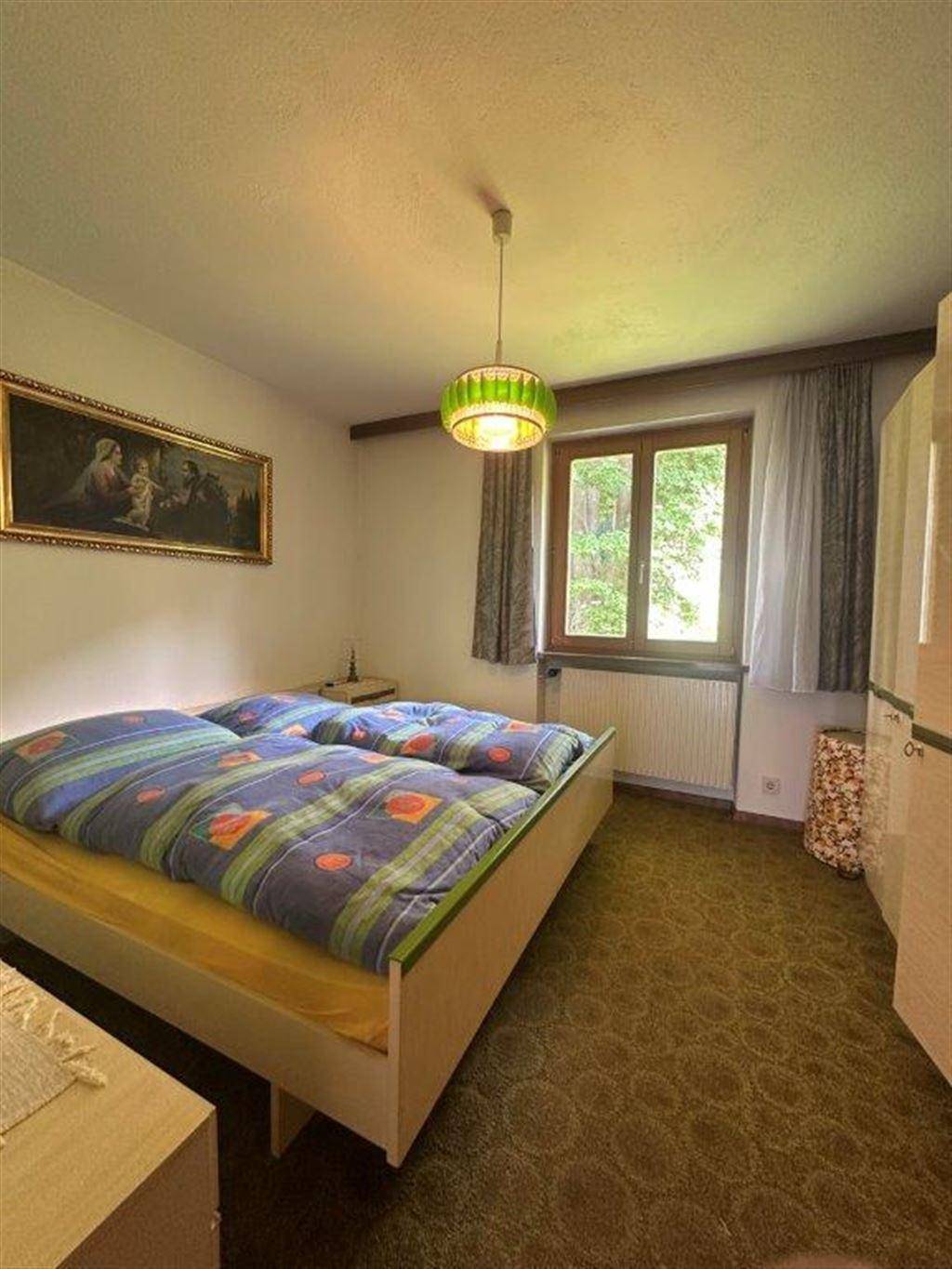 Schlafzimmer mit Teppichboden, Doppelbett und einem Fenster mit Blick ins Grüne.