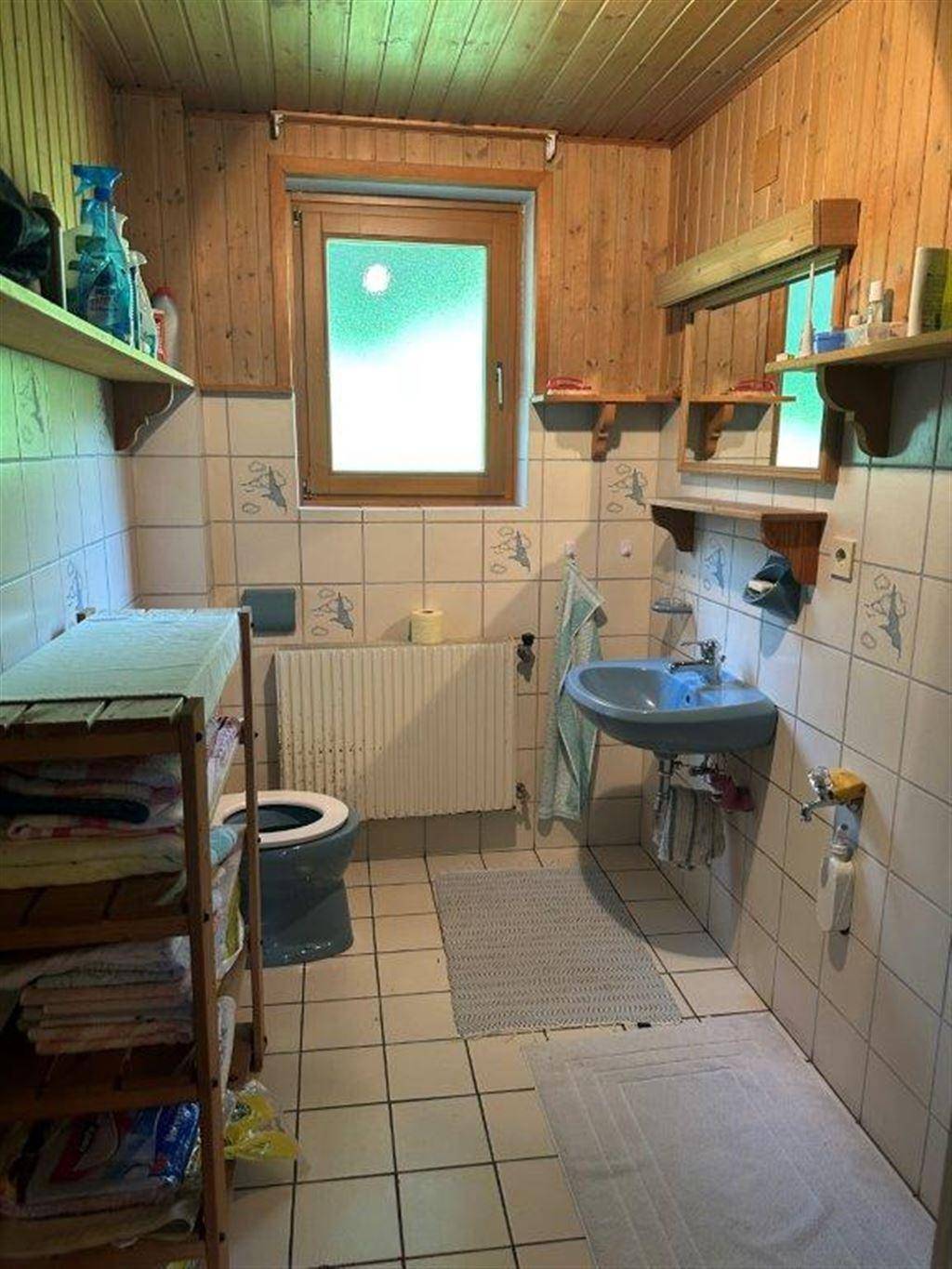 Kleines Badezimmer mit Holzvertäfelung, Fliesenboden und Fenster für natürliche Belüftung.