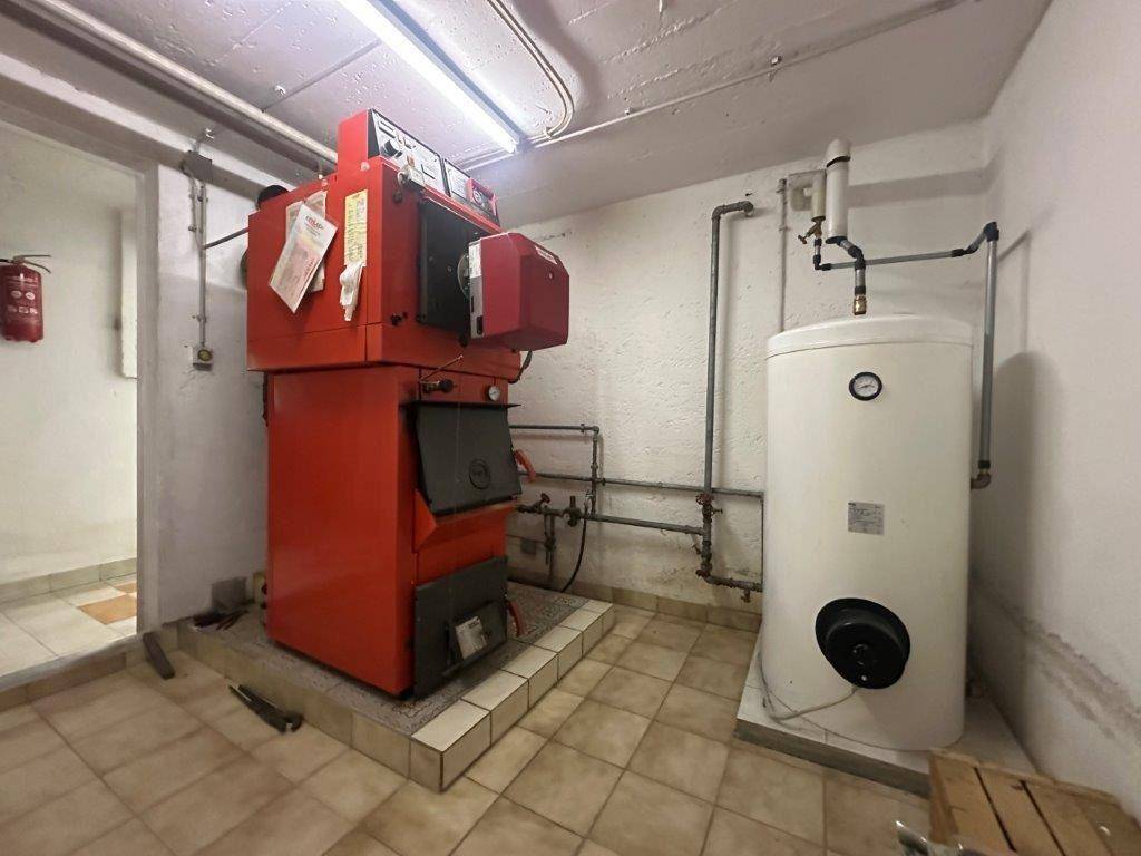 Heizungsraum mit großem roten Heizkessel und Warmwasserspeicher, typisch für ältere Anlagen.