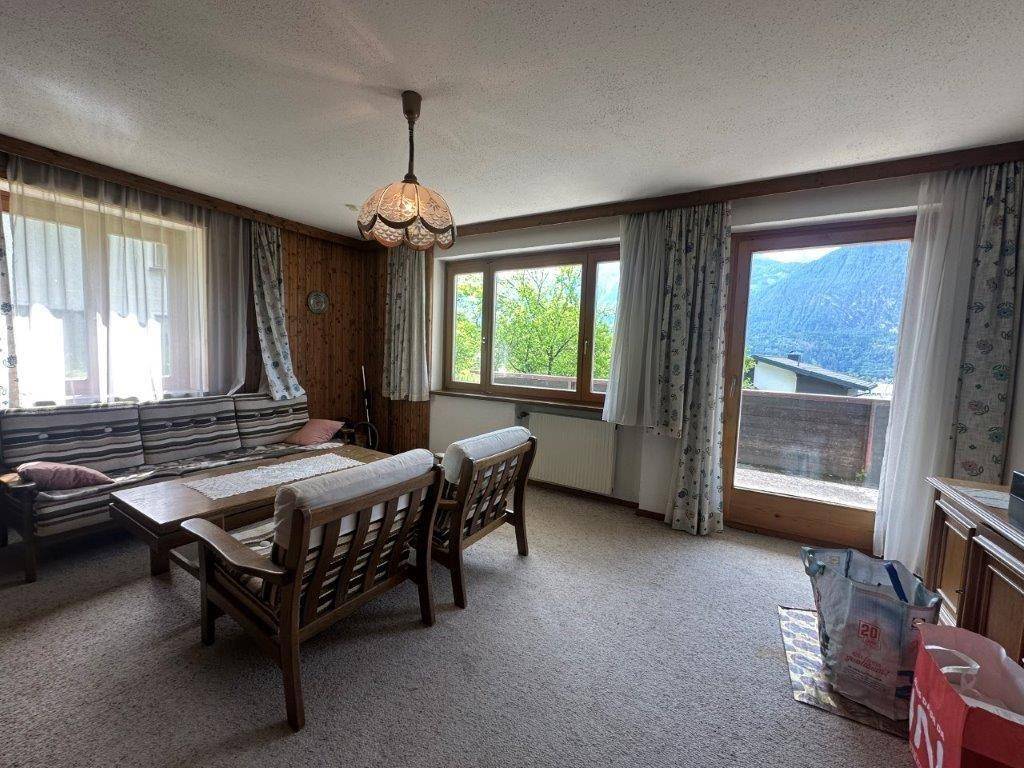Geräumiges Wohnzimmer mit Teppichboden, Holzvertäfelung und Zugang zu einem Balkon mit Bergblick.