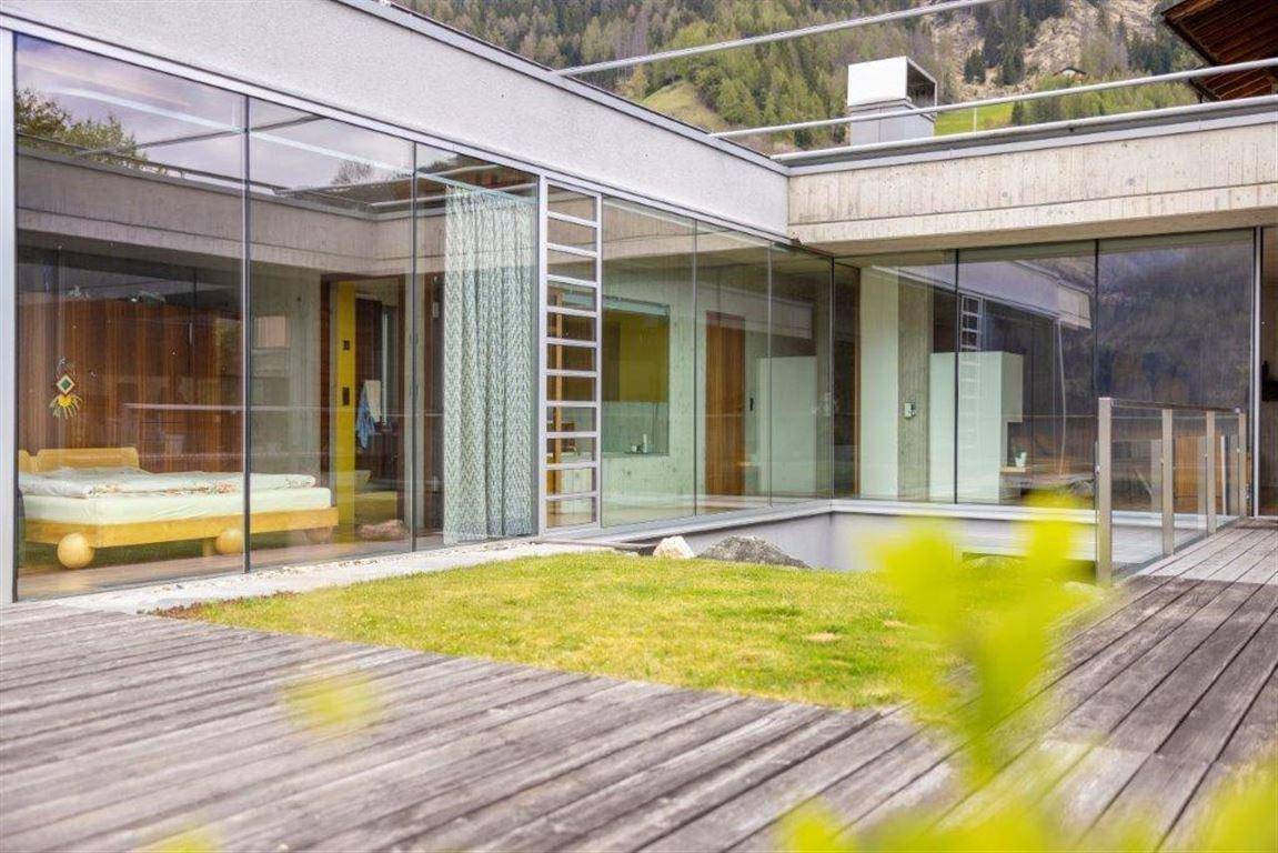 Weitläufige Holzterrasse mit Rasenfläche und Blick auf die Innenräume durch große Glasfronten.