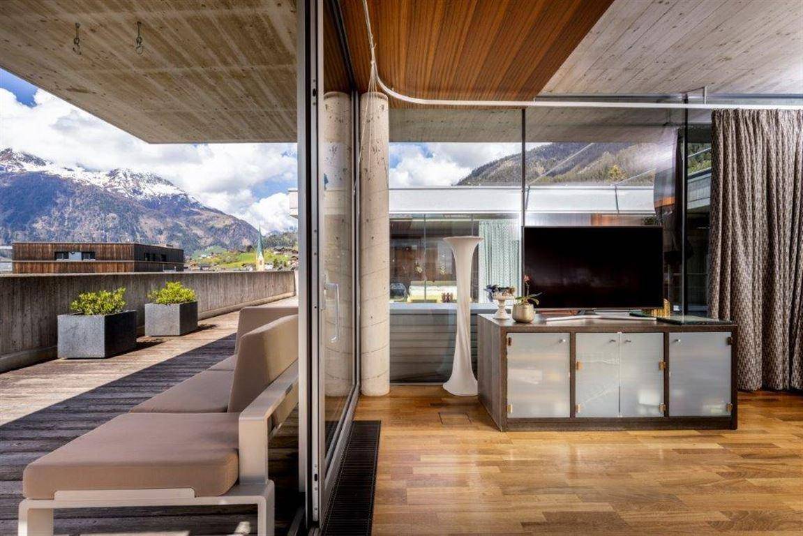 Heller Wohnbereich mit Holzboden, TV-Möbel und Zugang zu einer großen Terrasse mit Bergblick.