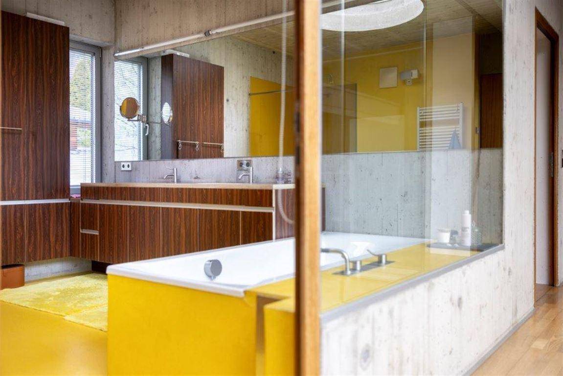 Modernes Badezimmer mit gelbem Boden, Doppelwaschbecken, Badewanne und Holzelementen.