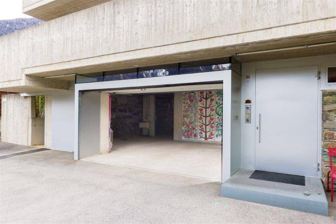 Geräumige Garage mit offenem Tor und Zugang zum Gebäude, daneben ein Eingangsbereich.