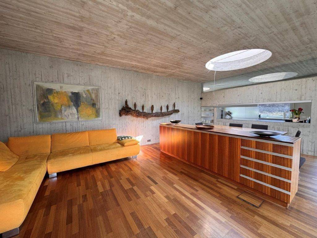 Offener Wohnbereich mit gelbem Sofa, Holzboden, Betonwänden und runden Oberlichtern.