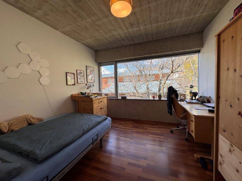 Helles Schlafzimmer mit Holzboden, Schreibtisch und großem Fenster mit Blick ins Grüne.