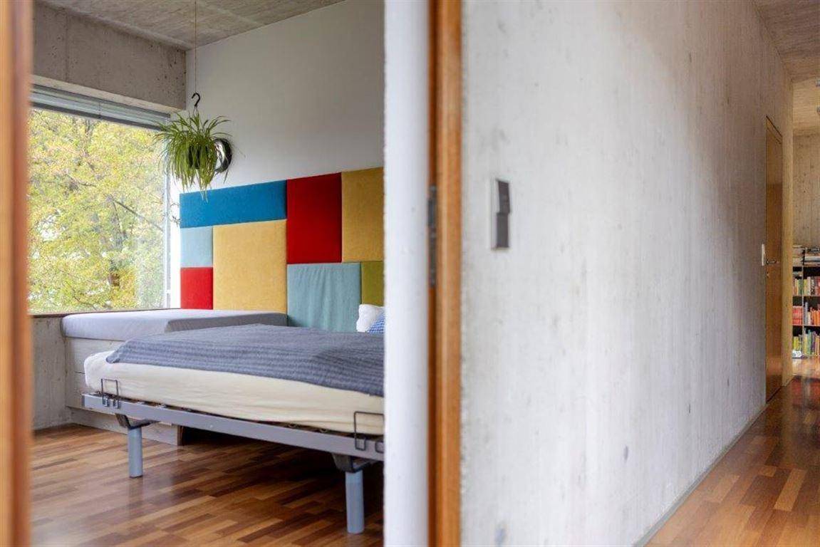 Schlafzimmer mit farbenfrohem Kopfteil, Holzboden und großem Fenster mit Blick nach draußen.