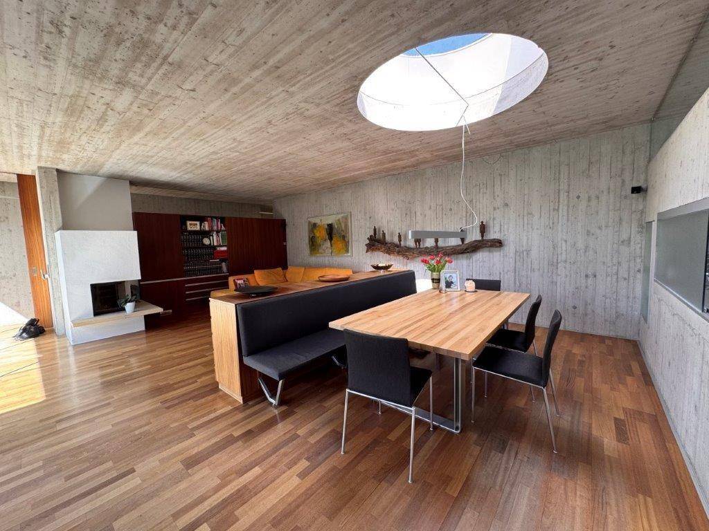 Offener Wohn-Essbereich mit Kamin, Holztisch, Holzboden und runden Oberlichtern.