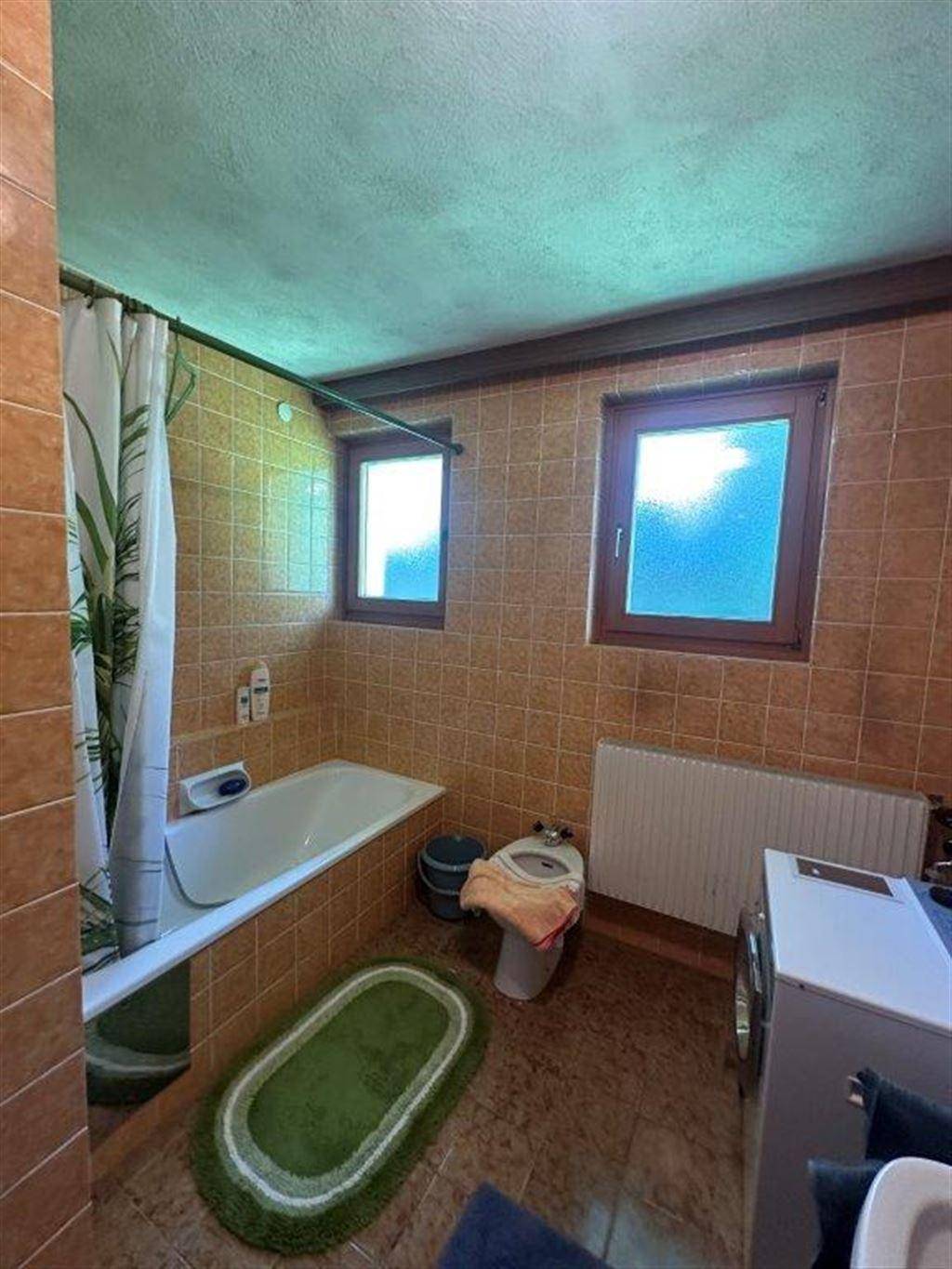 Badezimmer mit braunen Fliesen, Badewanne und Fenster, das Tageslicht hereinlässt.