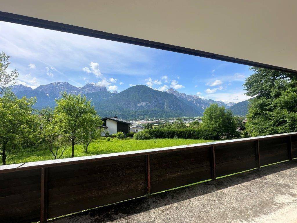 Blick vom Balkon auf eine weite grüne Landschaft mit Häusern und majestätischen Bergen im Hintergrund.