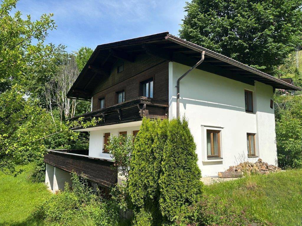 Traditionelles Haus mit weißer Fassade und Holzbalkonen, umgeben von üppigem Grün.