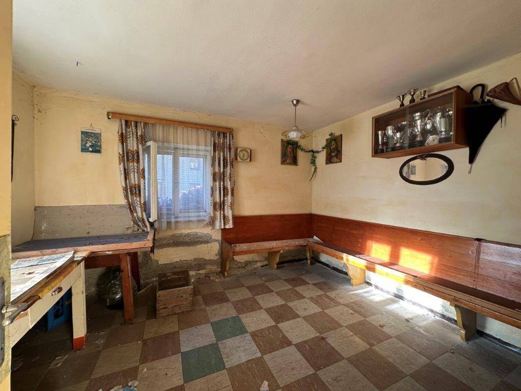 Rustikaler Wohnbereich mit Holzbänken, kariertem Boden und sichtbaren Gebrauchsspuren.