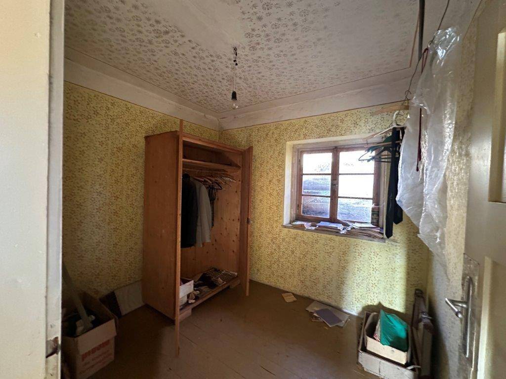Kleines Zimmer mit gemusterter Tapete und Holzschrank, ideal als Gäste- oder Abstellraum.