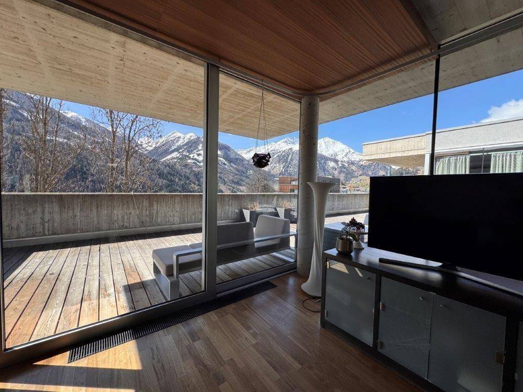 Helles Wohnzimmer mit Holzboden und raumhohen Fenstern, die Zugang zur Terrasse und Bergblick bieten.