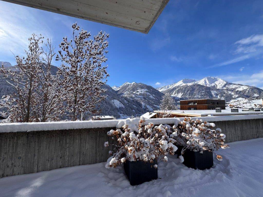 Verschneite Terrasse mit Topfpflanzen und weitem Blick auf die winterliche Berglandschaft.