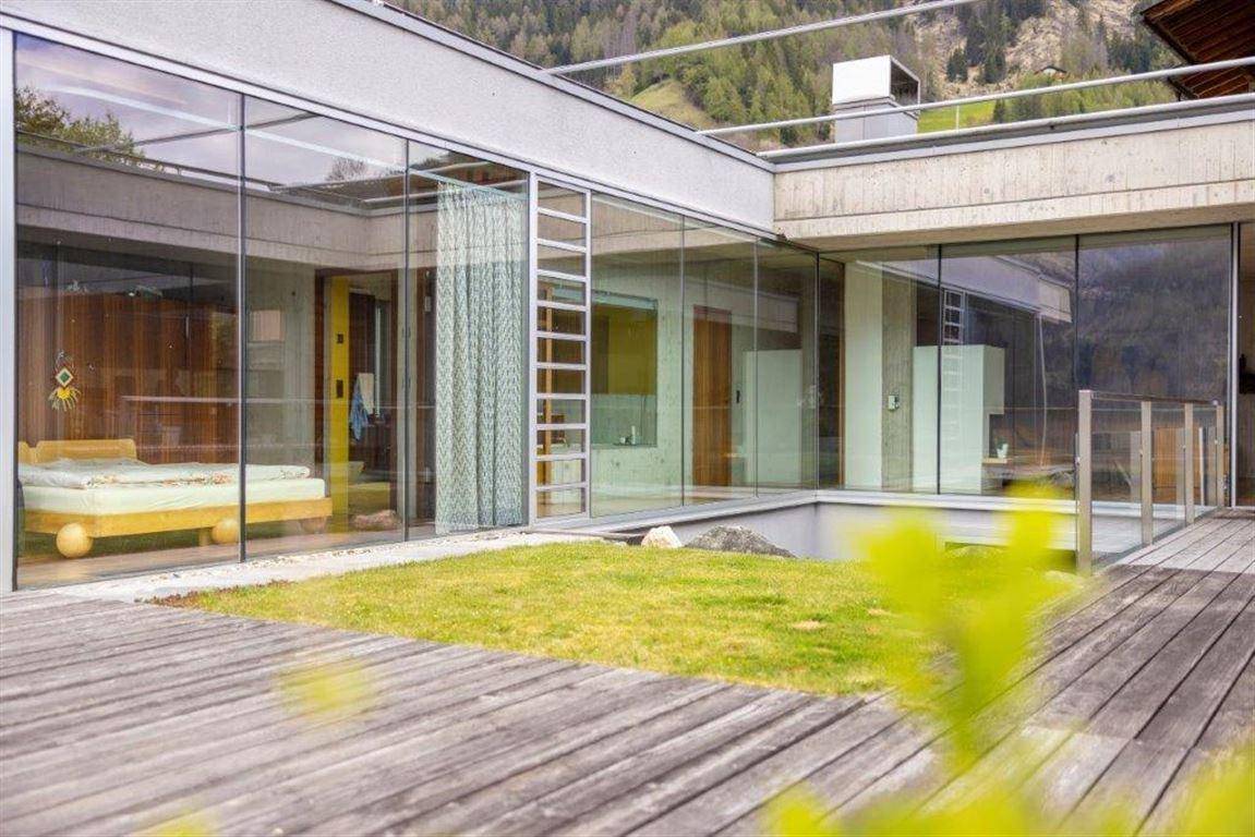 Großzügige Holzterrasse mit integrierter Rasenfläche und moderner Glasfassade, die den Innenbereich offenbart.