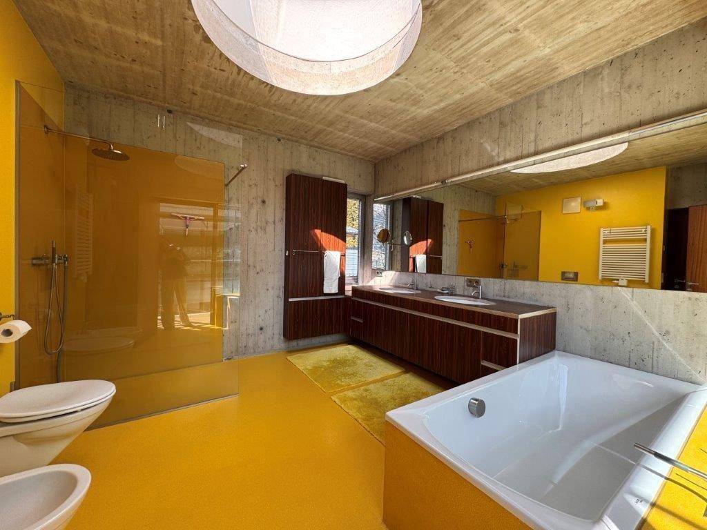 Großes Badezimmer mit gelbem Boden, Badewanne, Dusche und Doppelwaschbecken unter einem runden Oberlicht.