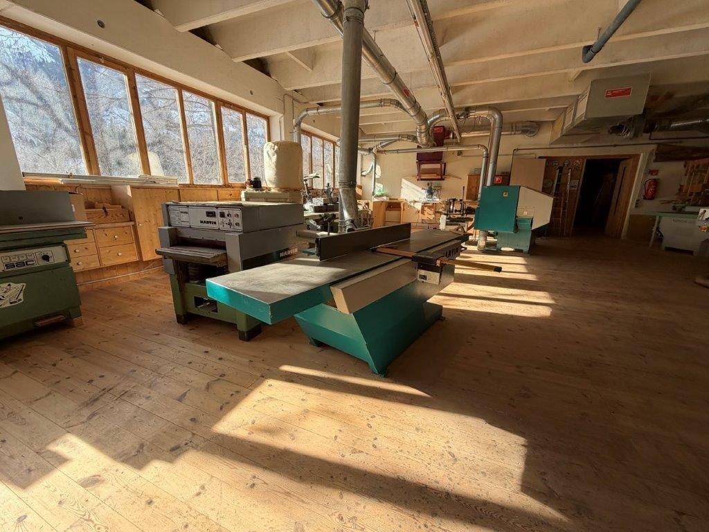 Werkstattraum mit verschiedenen Holzbearbeitungsmaschinen, großen Fenstern und Holzboden.