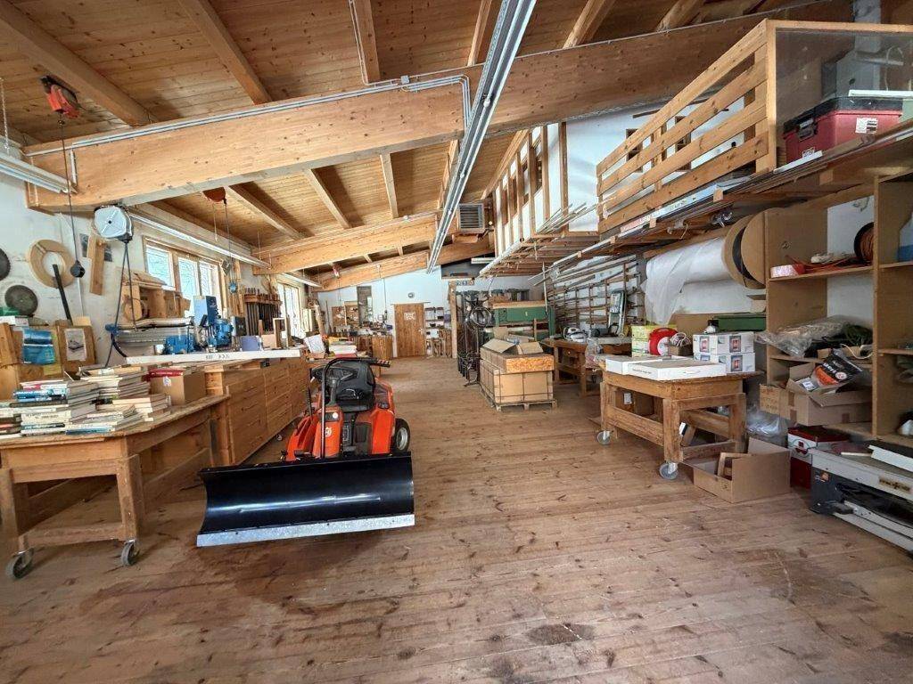 Geräumiger Werkstattbereich mit Arbeitsflächen, Lagerregalen und Holzfußboden, gut beleuchtet.
