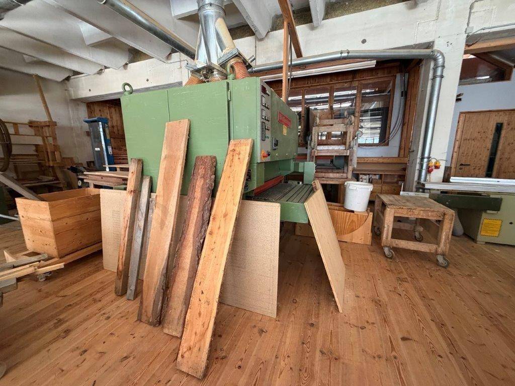 Werkstattraum mit Holzbearbeitungsmaschine und gestapelten Holzbrettern auf Holzboden.