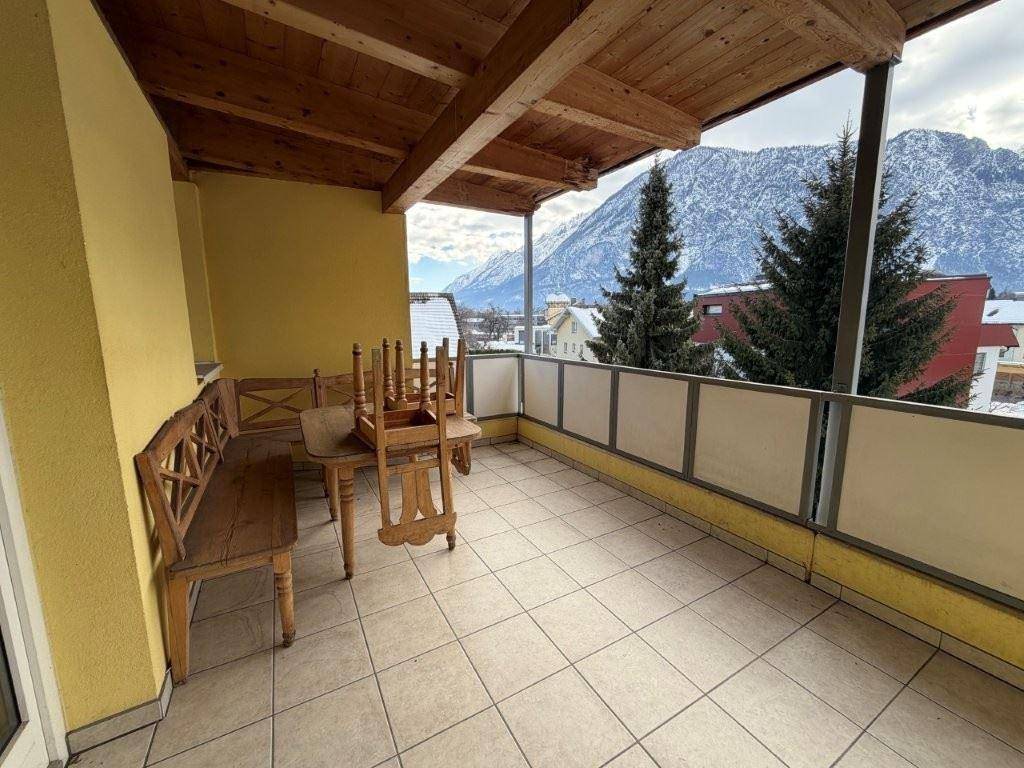 Geräumiger Balkon mit Fliesenboden, Holzbalkendecke und Panoramablick auf die schneebedeckten Berge.