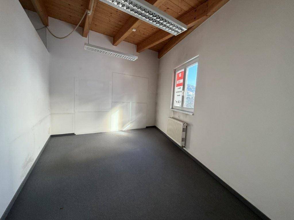 Leerer Büroraum mit schräger Decke, Holzbalken und einem Fenster mit Blick auf die Berge.