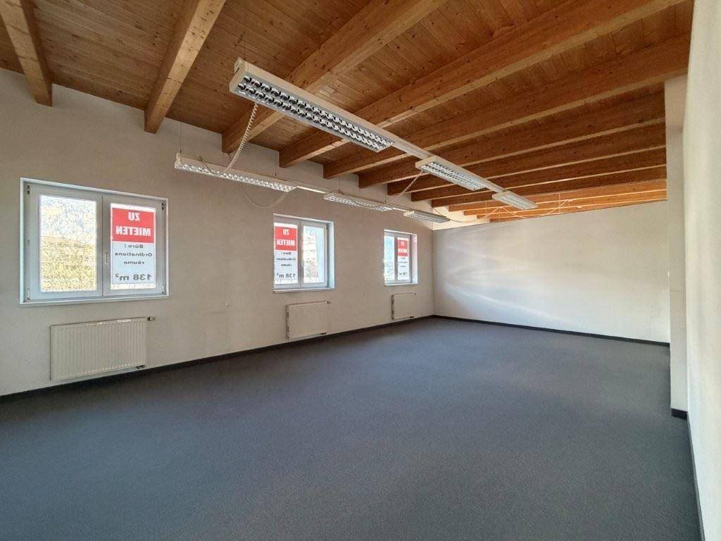 Heller Büroraum mit sichtbaren Holzbalken an der Decke und mehreren Fenstern für viel Tageslicht.