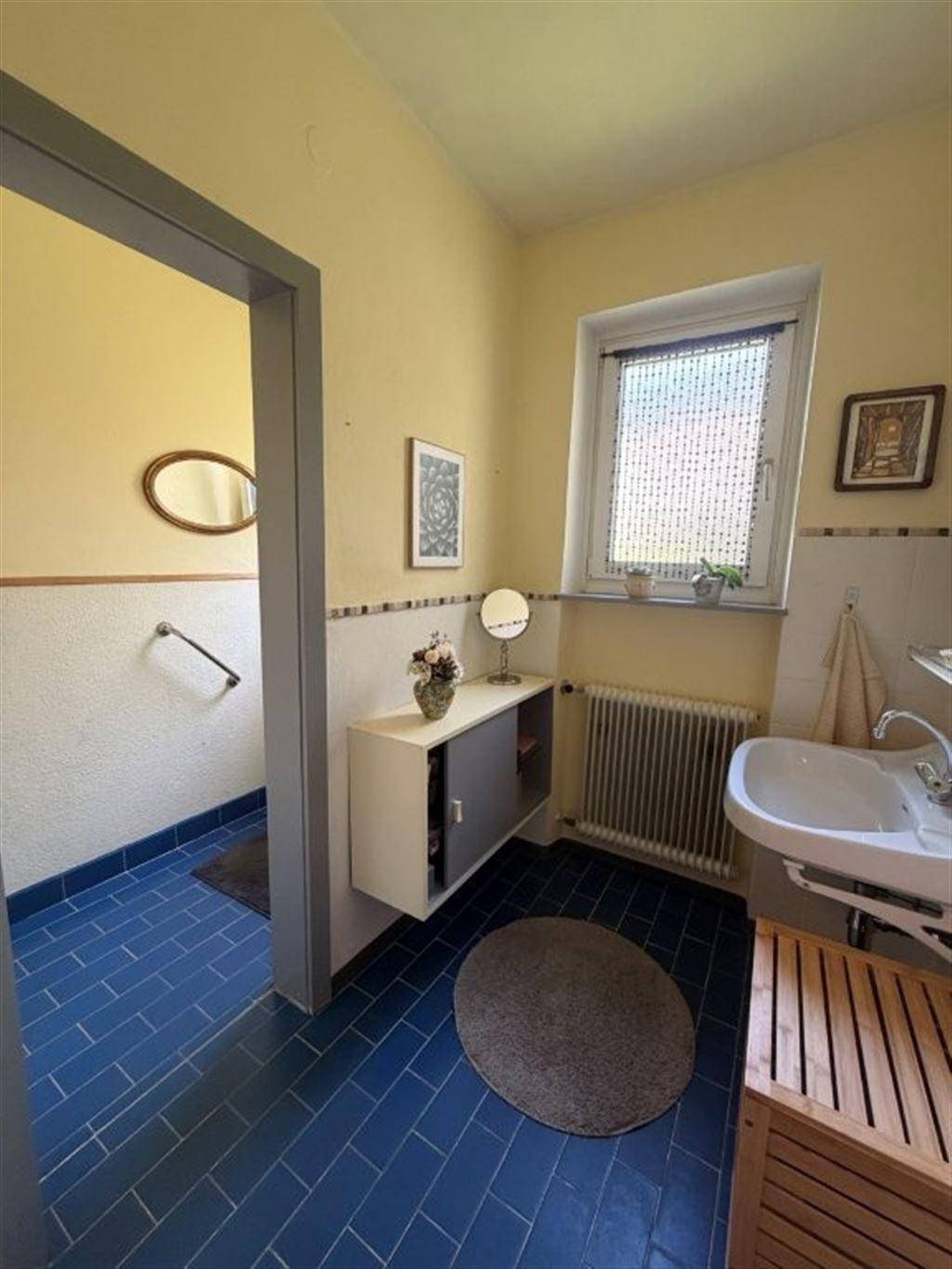 Badezimmer mit blauen Fliesen, gelben Wänden, Einzelwaschbecken und Fenster für Tageslicht.
