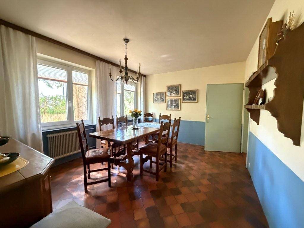 Gemütliches Esszimmer mit traditionellem Holztisch, Stühlen und Terrakottafliesen, hell durch große Fenster.