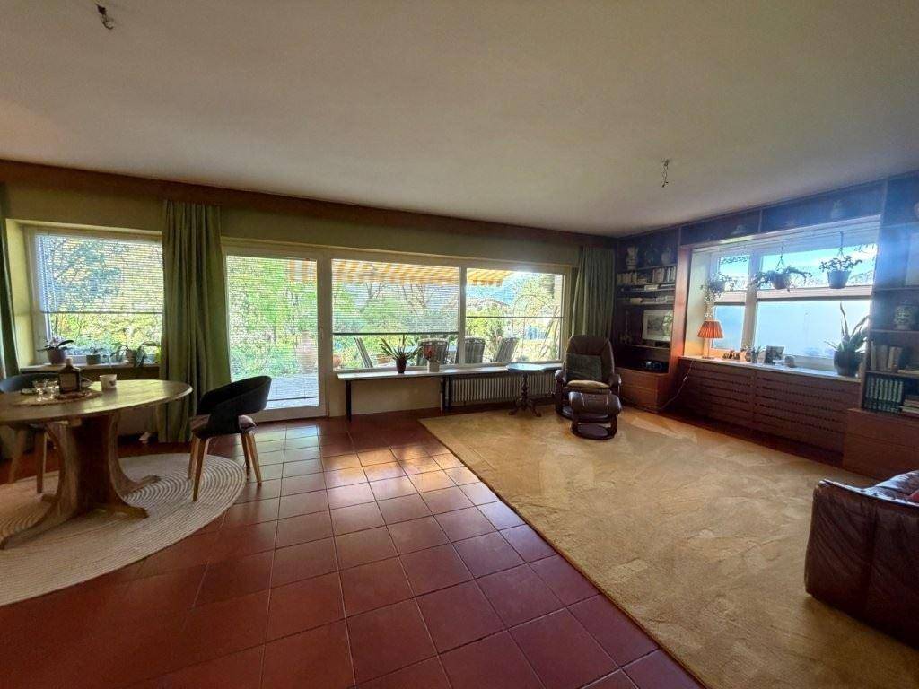 Geräumiges Wohnzimmer mit Terrakottafliesen, Teppich und großen Fenstern mit Blick ins Grüne.