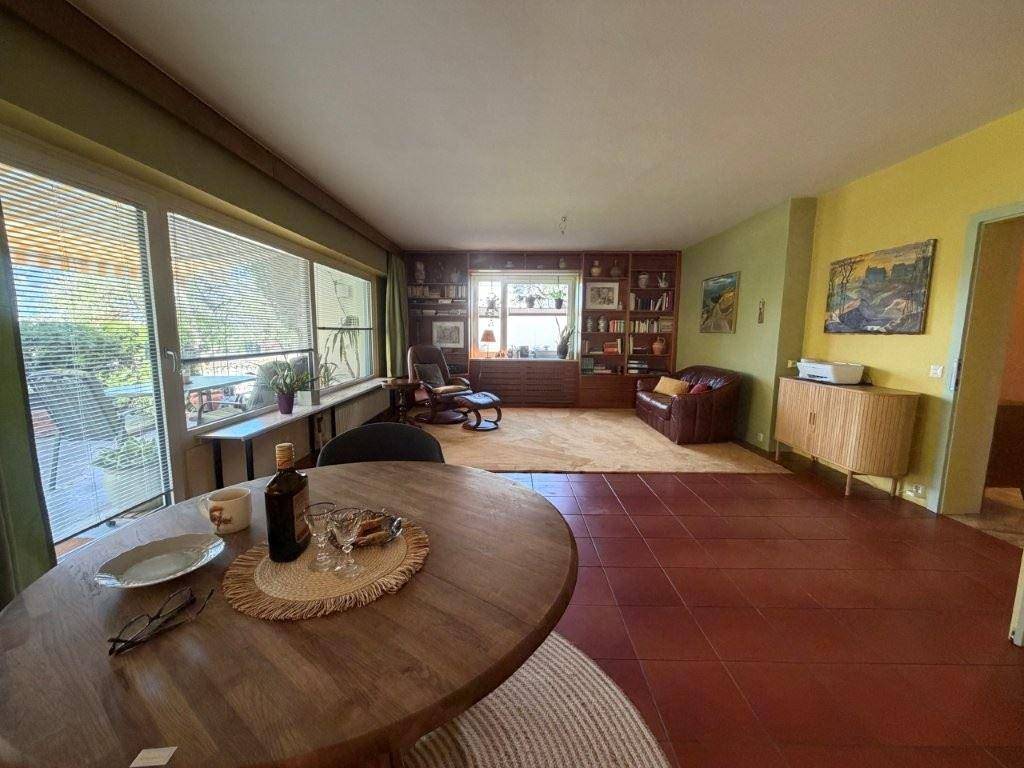 Helles Wohnzimmer mit Essbereich, Terrakottafliesen und großen Fenstern mit Blick ins Grüne.