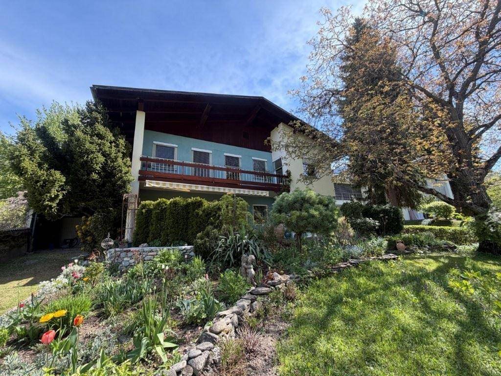 Charmantes Haus mit Balkon und einem blühenden Vorgarten, umgeben von Bäumen und Natur.