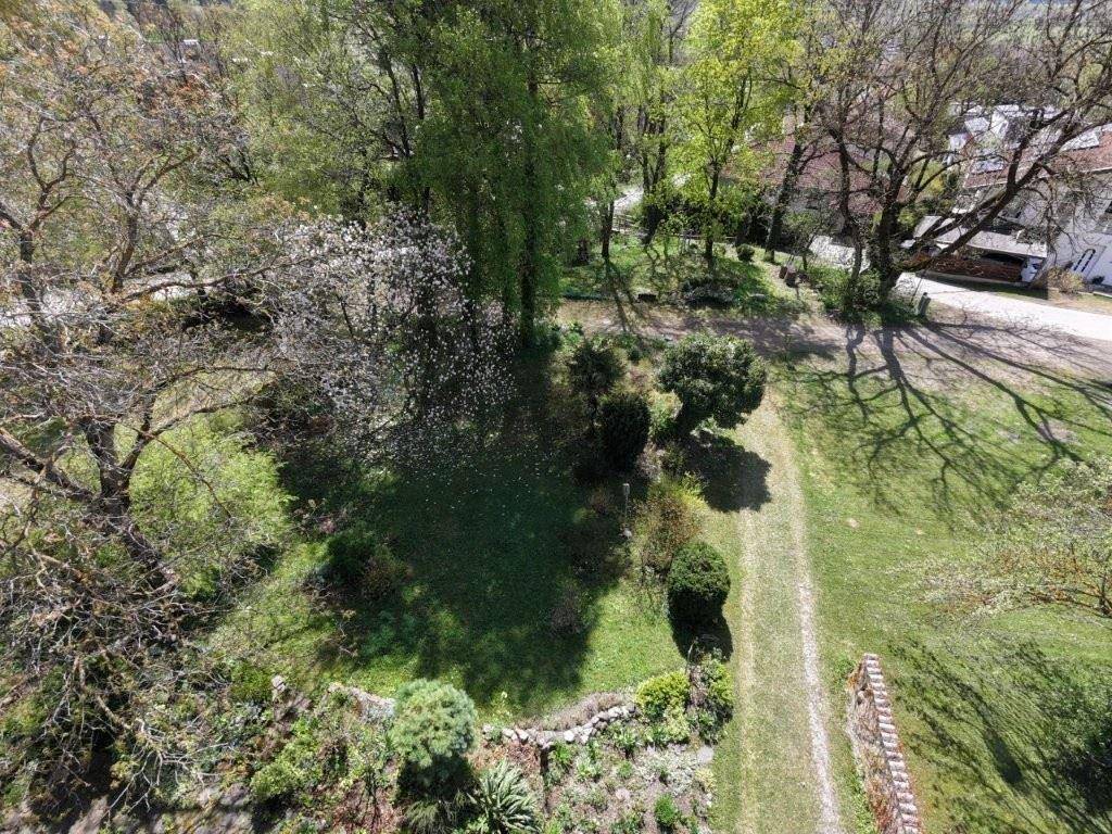 Vogelperspektive auf den weitläufigen, grünen Gartenbereich mit altem Baumbestand und Blumenbeeten.