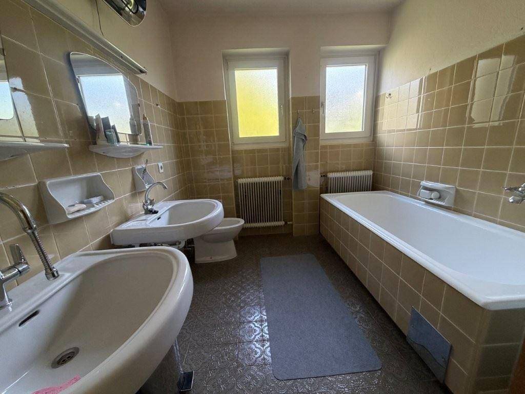 Klassisches Badezimmer mit zwei Waschbecken, Badewanne und beigefarbenen Fliesen aus den 80ern.
