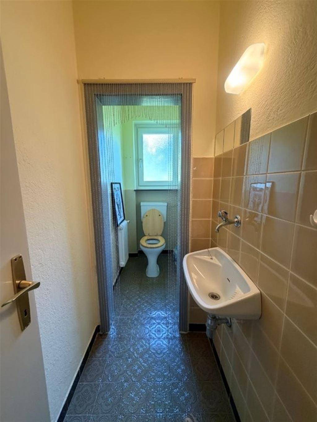 Separate Gästetoilette mit kleinem Waschbecken und beigefarbenen Fliesen.