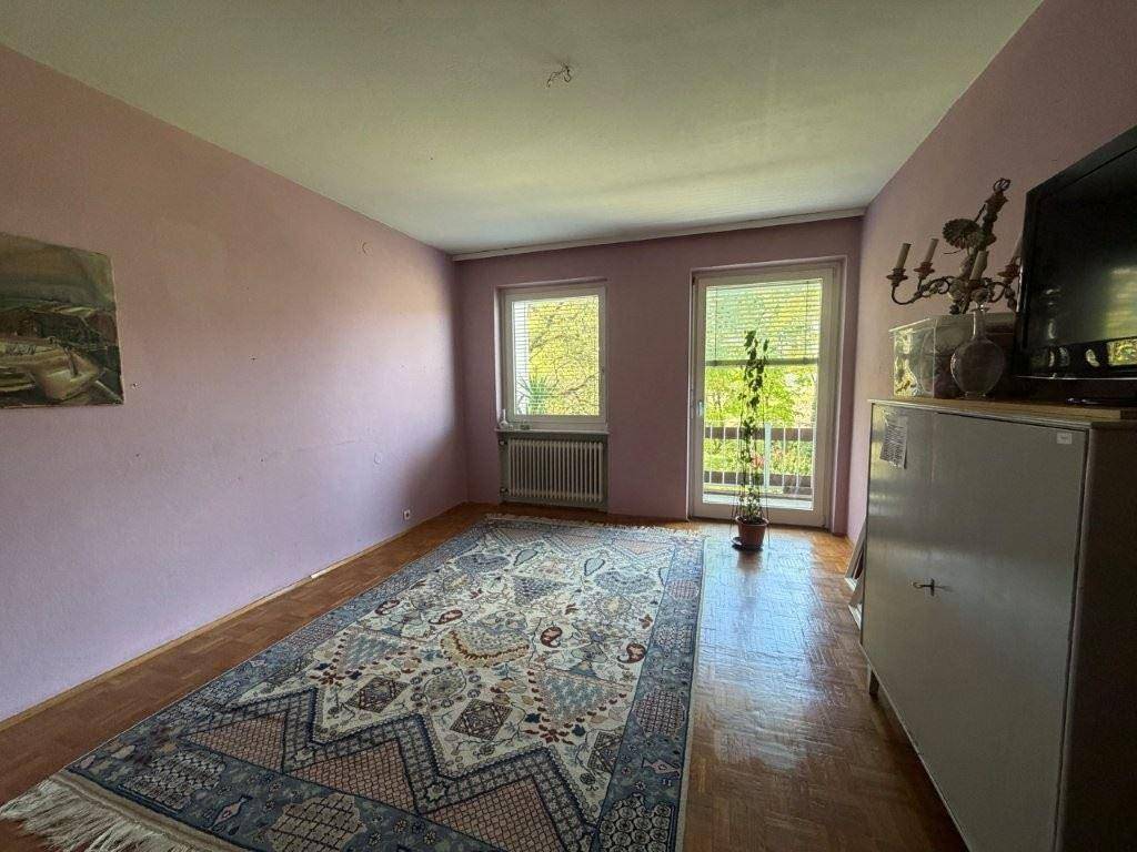 Helles Schlafzimmer mit Parkettboden, Teppich und Zugang zu einem französischen Balkon.
