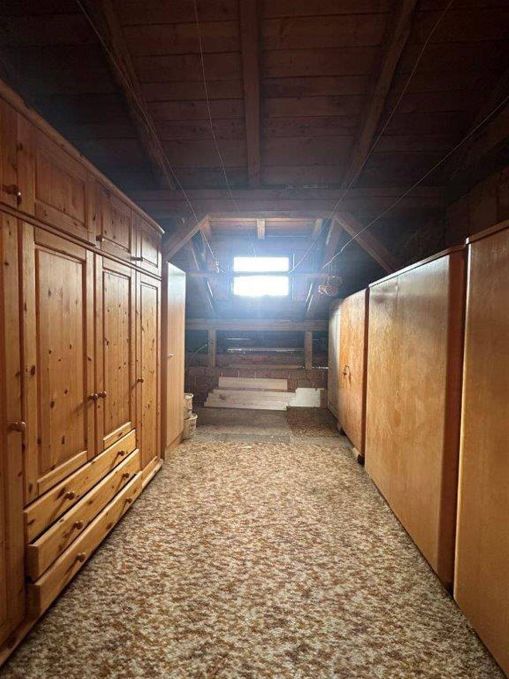Dachboden als Stauraum genutzt, mit sichtbaren Holzbalken, Dachschrägen und einem kleinen Fenster.