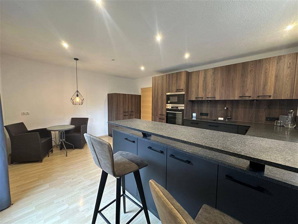Moderne Küche mit dunklen Holzschränken, Kücheninsel und angrenzendem Ess- oder Loungebereich.
