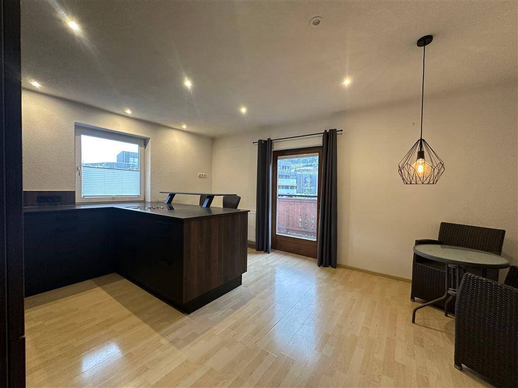 Offener Wohnbereich mit moderner Kücheninsel, hellem Holzboden und Zugang zu einem Balkon.