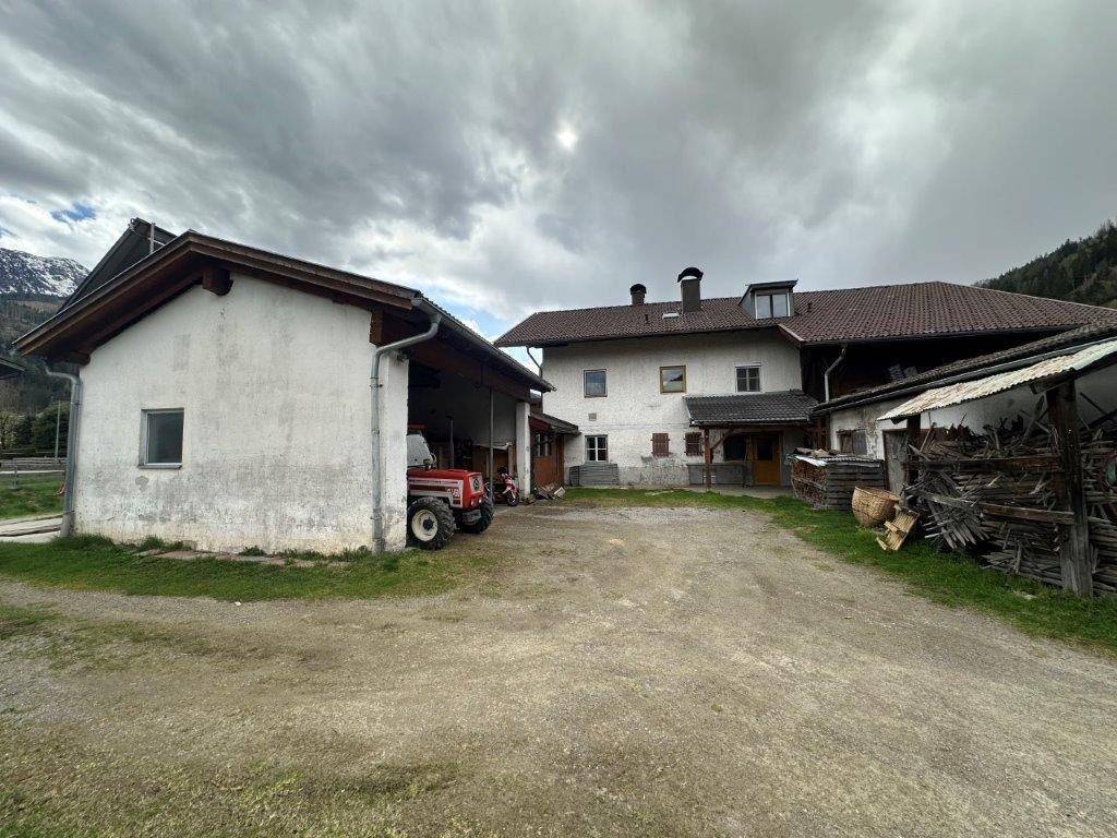 Ländliches Anwesen mit mehreren Gebäuden, darunter ein Bauernhaus und eine Scheune, umgeben von Natur.