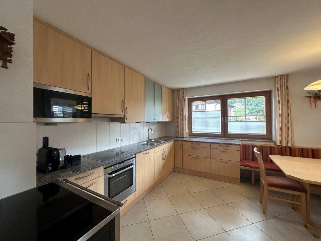 Helle Küche mit Holzschränken, Granitarbeitsplatte, Fliesenboden und gemütlicher Essecke am Fenster.