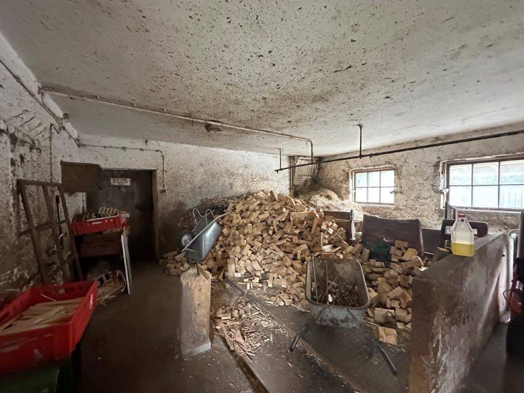 Kellerraum oder Lagerbereich gefüllt mit Brennholz, mit rauen Betonwänden und kleinen Fenstern.