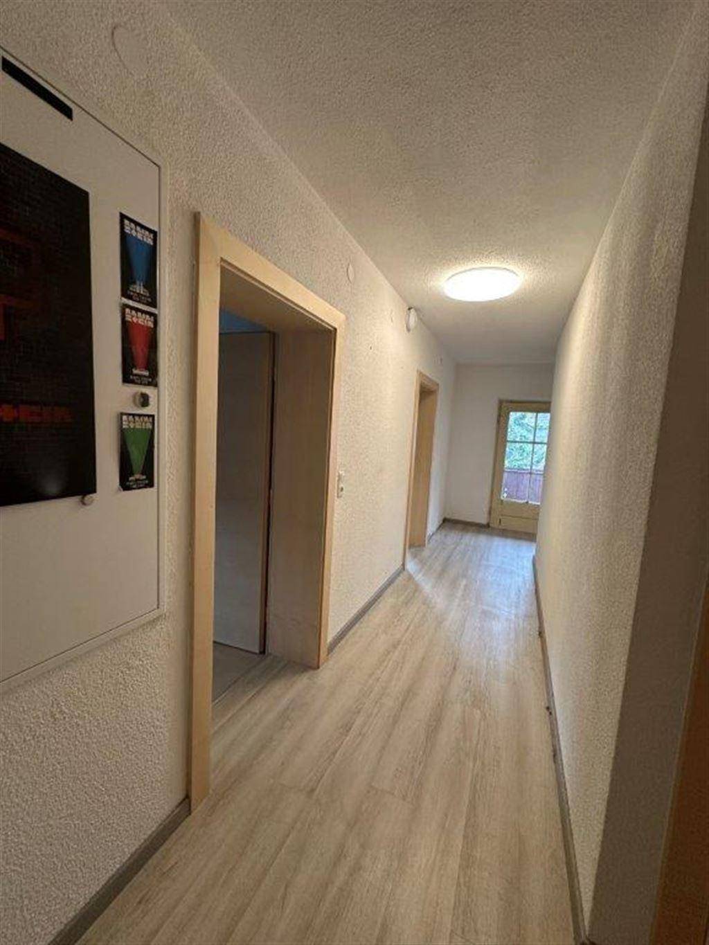 Heller Flur mit Laminatboden in Holzoptik und weißen Wänden, führt zu einer Außentür.