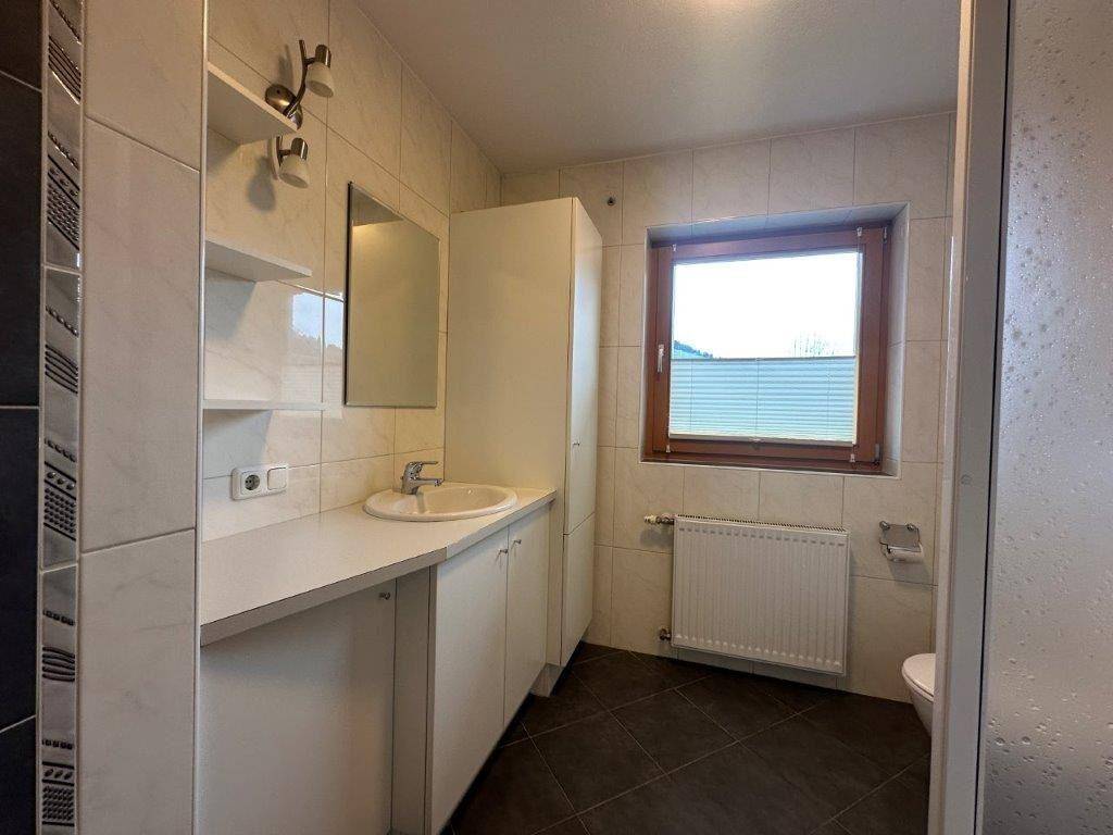 Modernes Badezimmer mit weißen Wandfliesen, Waschbecken, WC und Fenster für natürliche Belüftung.