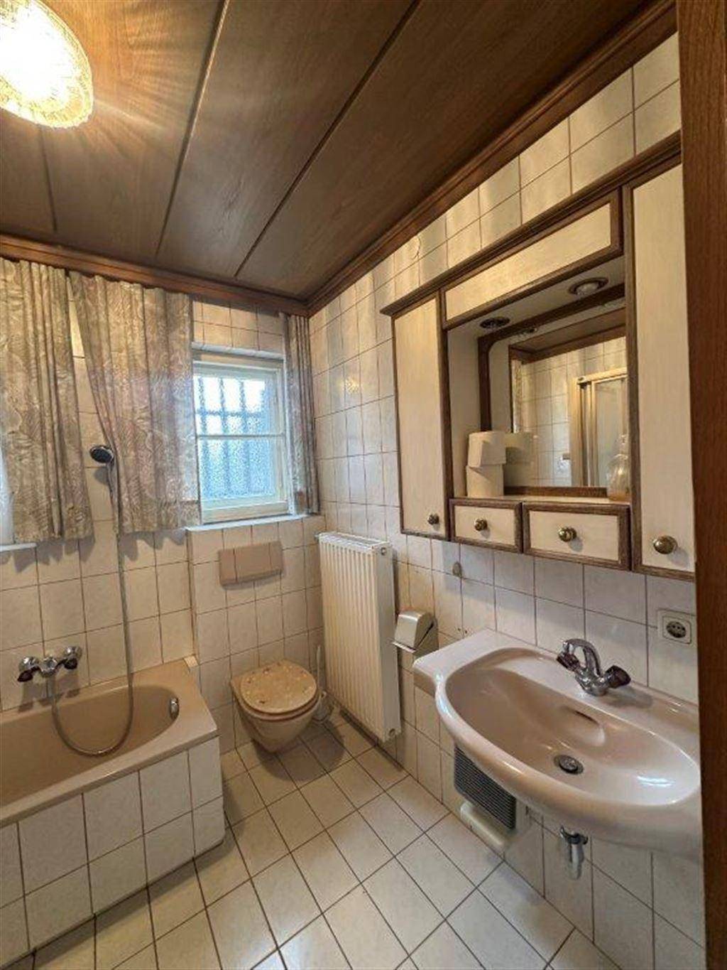Badezimmer im 80er-Jahre-Stil mit beigen Fliesen, Badewanne, Waschbecken und Spiegelschrank.