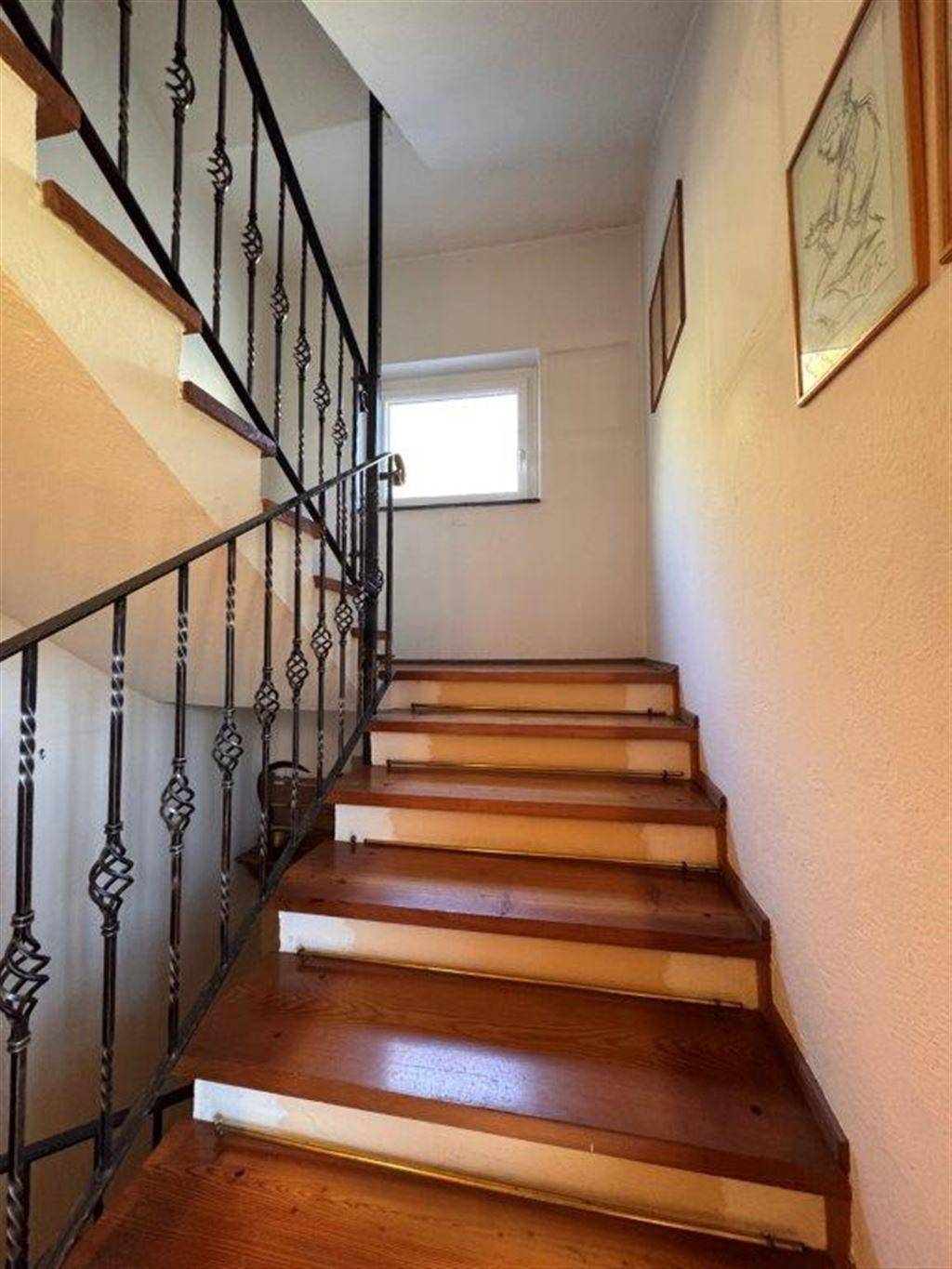 Holztreppe mit schmiedeeisernem Geländer und Fenster, die die Stockwerke verbindet.